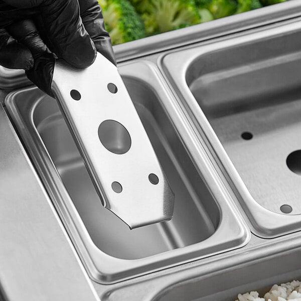 A hand holding a stainless steel Choice steam table pan false bottom.