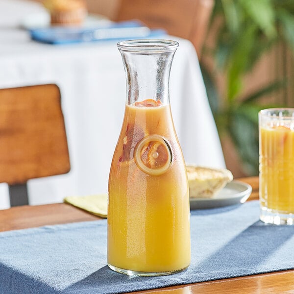 An Anchor Hocking glass carafe filled with orange juice on a table.