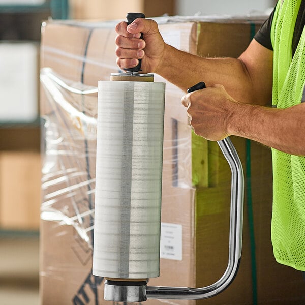 A man in a safety vest using 18" x 1500' 70 gauge hand pallet wrap to wrap a pallet.
