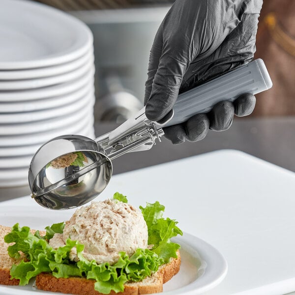 A person in gloves using a Choice Gray Thumb Press Disher to scoop food onto a plate.