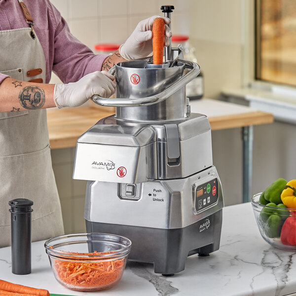 A person using an AvaMix motor base to shred carrots in a bowl.