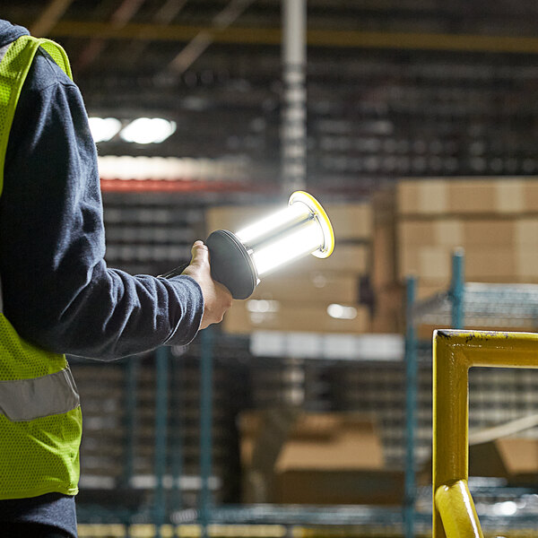 A person in a yellow vest holding a Lind Equipment Beacon360 LED portable hand lamp.