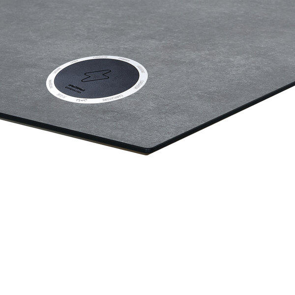 A close-up of a grey BFM Seating round table top with a white wireless charger.