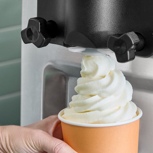 A close up of a hand holding a cup with white swirly soft serve on top.