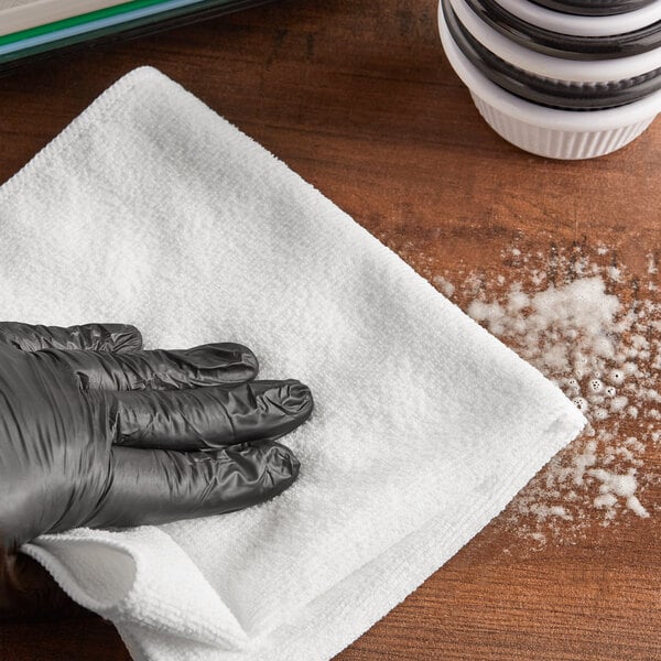 A hand in a black glove cleaning a white Lavex microfiber cloth.