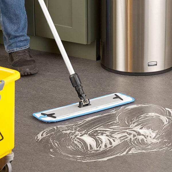 A person mopping the floor with a yellow Lavex 18" Microfiber Hook & Loop Wet / Dry Mop Frame.