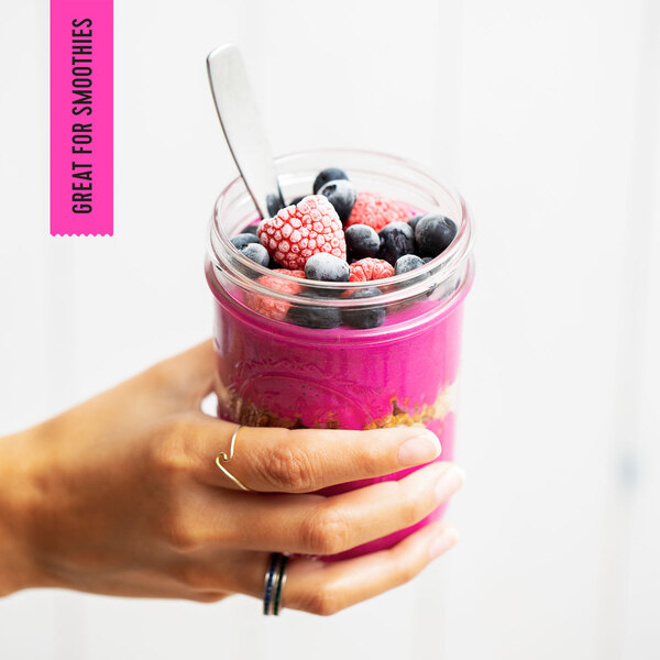 A hand holding a pink Pitaya Foods smoothie jar.