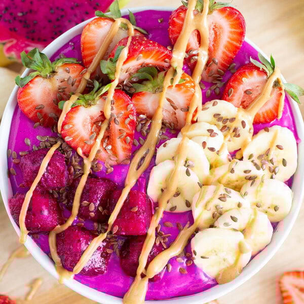 A bowl of Pitaya Foods organic dragon fruit smoothie next to a bowl of fruit and peanut butter.