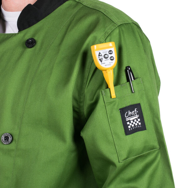 A person wearing a mint green Chef Revival chef jacket with a yellow pen in the pocket standing in a professional kitchen.