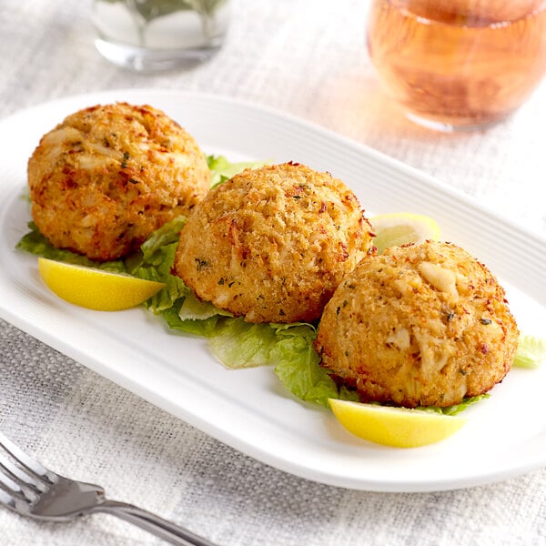 Three Handy crab cakes on a white plate with a lemon wedge.