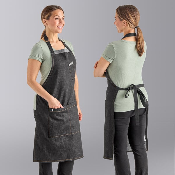 Two women wearing black Uncommon Chef denim aprons standing in a professional kitchen.