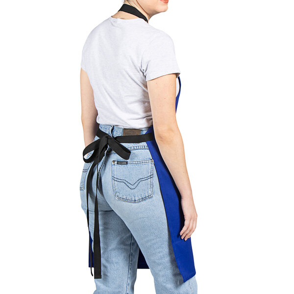 A woman wearing a Uncommon Chef Deep Royal blue bib apron with black webbing.