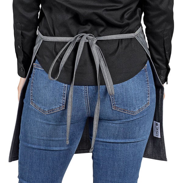 A woman wearing blue jeans and a black shirt using a grey Uncommon Chef waist apron with black webbing.