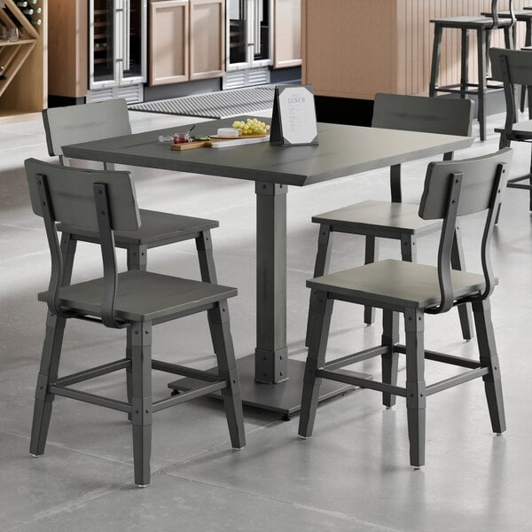 A square slate gray solid wood table with a live edge and four matching industrial-style chairs.