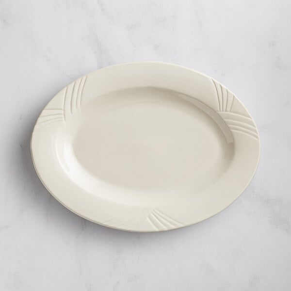 An Acopa ivory stoneware oval platter with an embossed design on the rim on a marble surface.