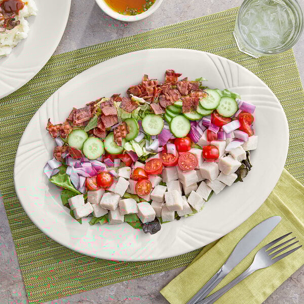An Acopa ivory stoneware oval platter with salad, meat, and a side dish on it.