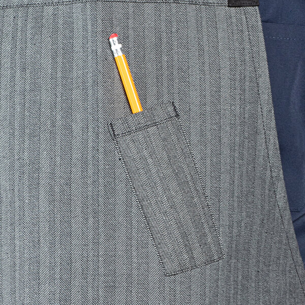 A pencil in a pocket of a grey denim bib apron.