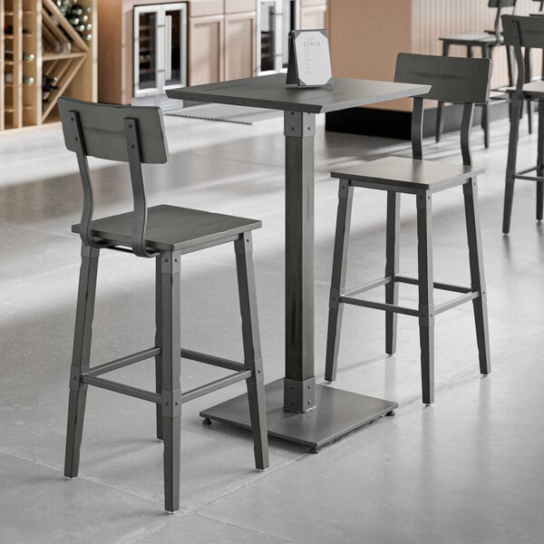 A Lancaster Table and Seating industrial bar height table with a live edge wood top and two bar stools with slate gray seats.