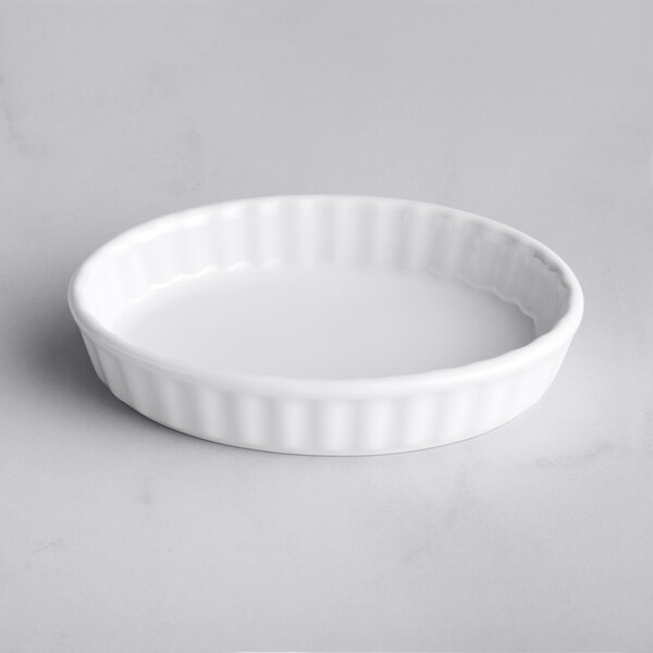 A Tuxton white porcelain fluted oval creme brulee dish on a white surface.