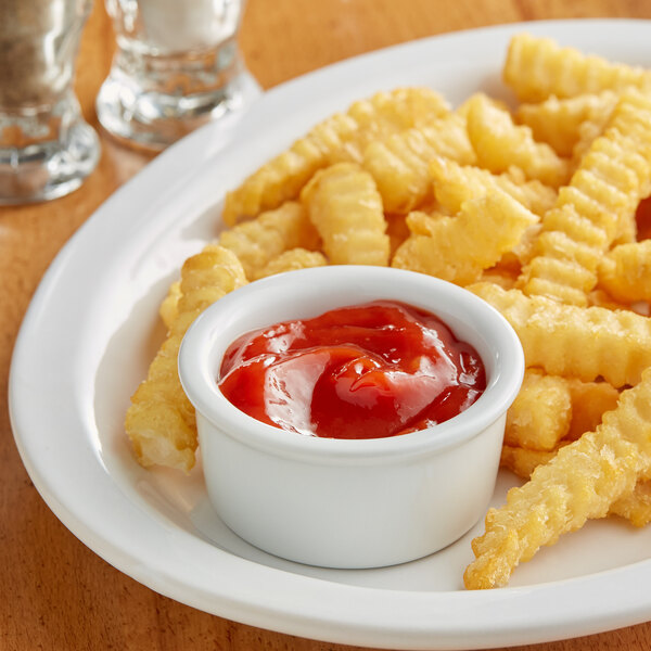 A plate of french fries with a Tuxton porcelain ramekin of ketchup.