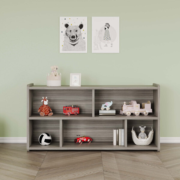 A Tot Mate Shadow Elm laminate toddler compartment storage unit with toys and a stuffed bear on the shelves.