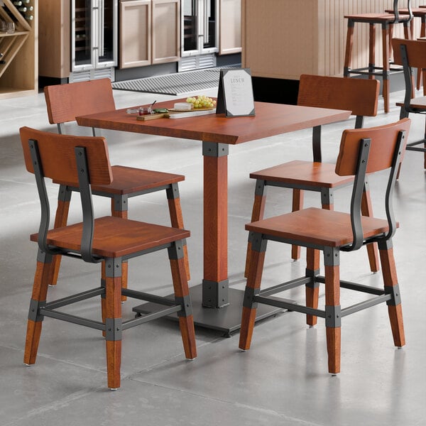 A square rustic mahogany finish wood table with four matching industrial-style chairs.
