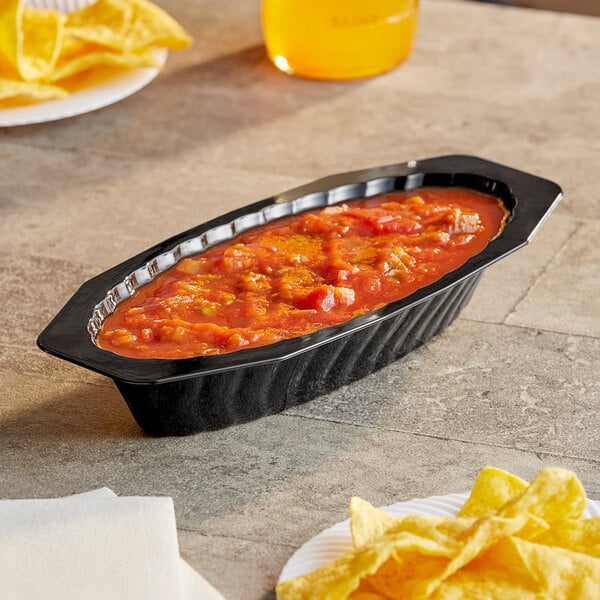 A black Fineline Flairware oval bowl filled with red sauce on a table.