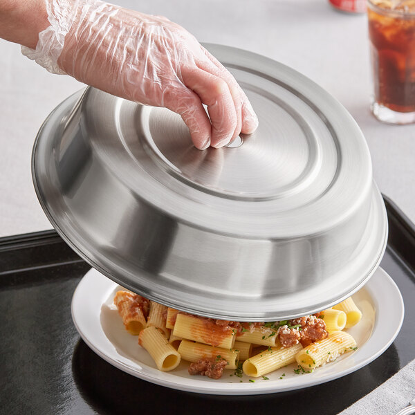 A hand holding an American Metalcraft stainless steel plate cover over a plate of pasta.