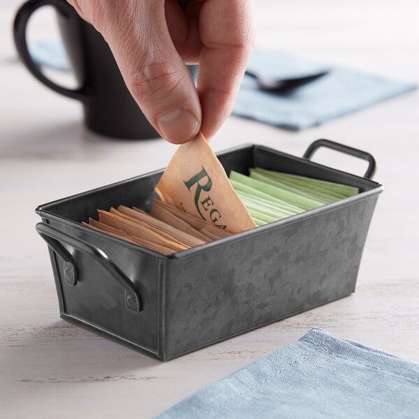 A person putting a packet of sugar into a black metal container.