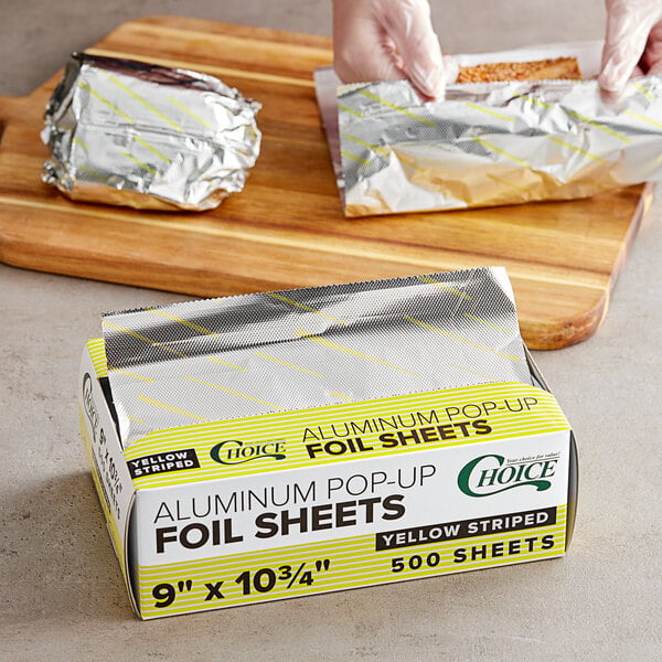 A person cutting Choice yellow striped interfolded foil sheets with a knife.