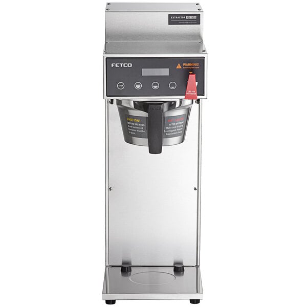 A Fetco airpot coffee maker with a large metal brew basket and black handle on a stainless steel stand.