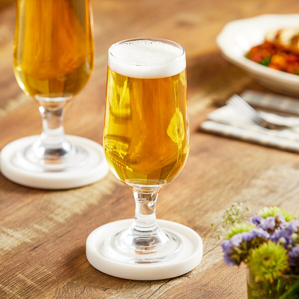 Two Acopa Select stemmed pilsner glasses of beer on coasters.