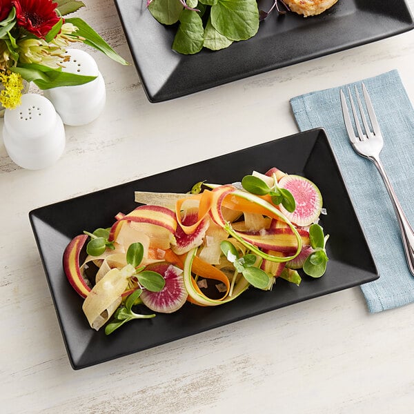 A rectangular matte black stoneware platter with food and a fork on it.