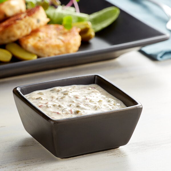 A white Acopa stoneware sauce cup filled with white sauce next to a plate of food.