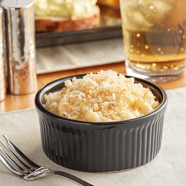 A black Acopa fluted stoneware dish filled with food on a table with a fork next to it.