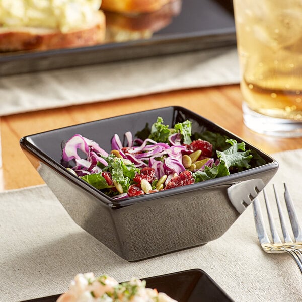 A bowl of salad in a black Acopa stoneware bowl on a table.