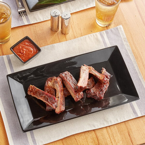 A piece of meat on an Acopa rectangular black stoneware platter with a glass of beer.