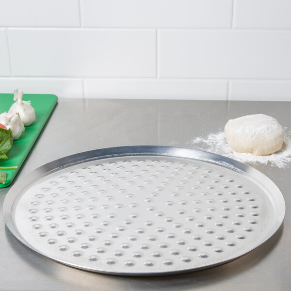 An American Metalcraft aluminum pizza pan with nibs next to a ball of dough.