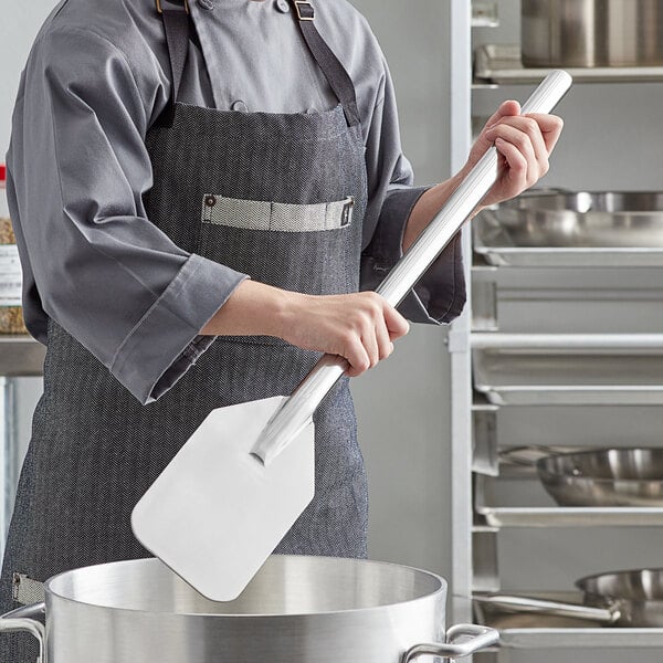 A person in a kitchen using an American Metalcraft stainless steel paddle to stir food in a pot.