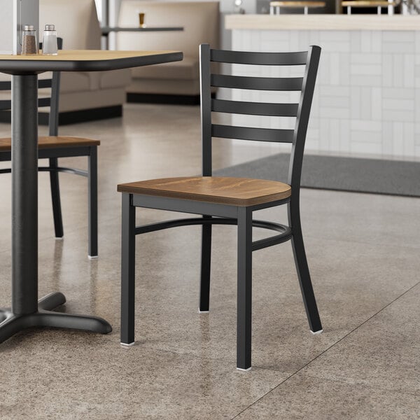 A Lancaster Table & Seating Black Finish Ladder Back Chair with Vintage Wood Seat on a table in a restaurant.