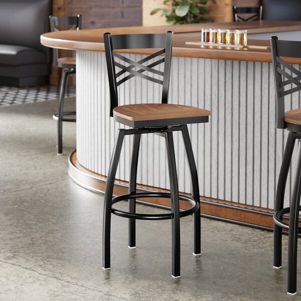 A black metal bar stool with a cross back design and a vintage wood seat.