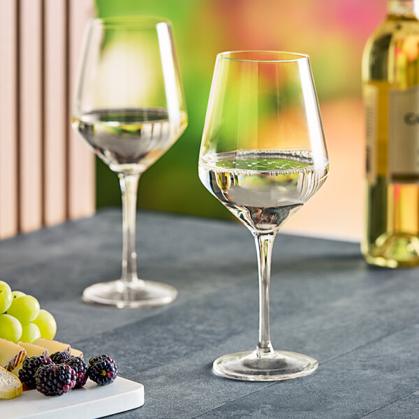 Two Acopa Silhouette wine glasses filled with wine next to a plate of grapes and a bottle.