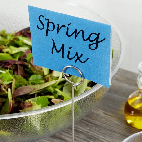 A bowl of salad with a stainless steel menu card holder in it.