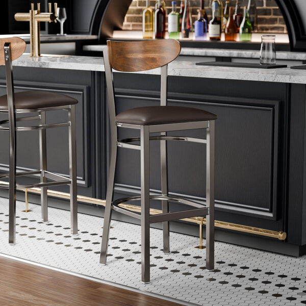 Two Lancaster Table & Seating Boomerang bar stools with a brown vinyl seat at a bar counter.
