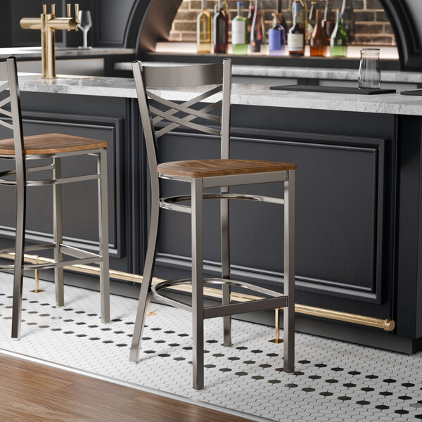 A metal bar stool with a cross back design and a vintage wood seat.