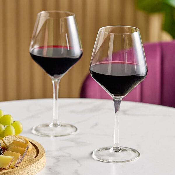 Two Acopa Silhouette wine glasses filled with red wine on a table.