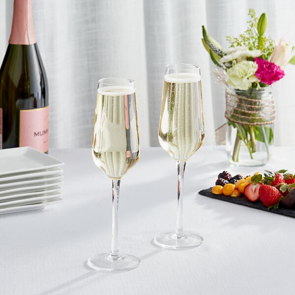 Two Acopa Silhouette champagne flutes on a table with a bouquet of flowers.