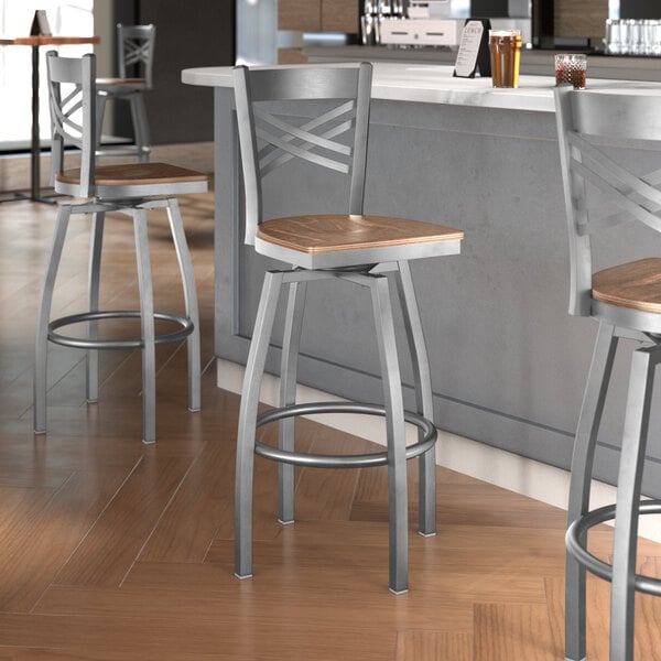A Lancaster Table & Seating swivel bar stool with a wooden seat and metal back.