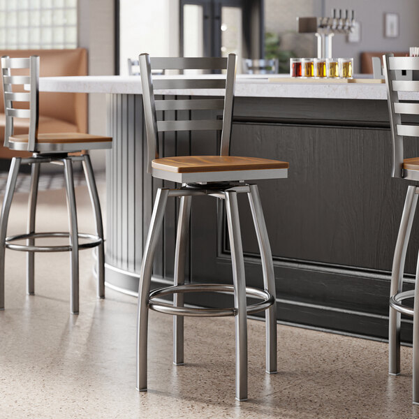 A group of Lancaster Table & Seating Ladder Back Swivel Bar Stools with vintage wood seats at a counter.