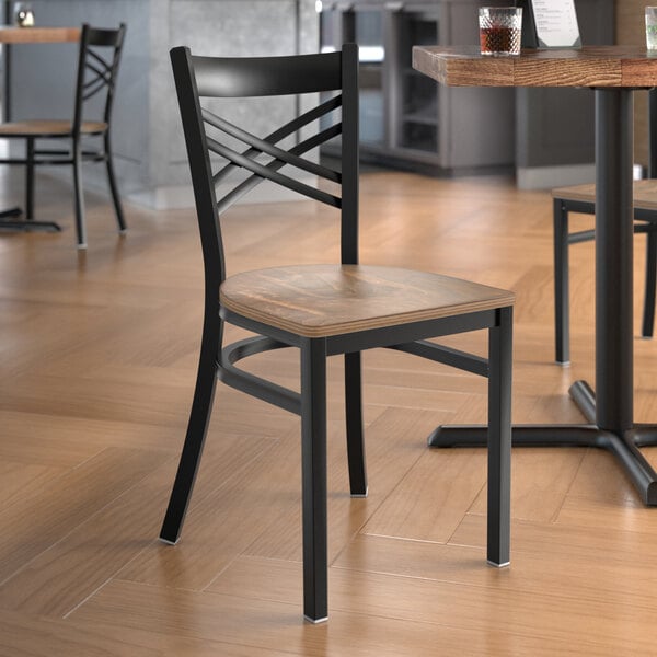 A Lancaster Table & Seating black metal cross back chair with a vintage wood seat at a table in a restaurant.